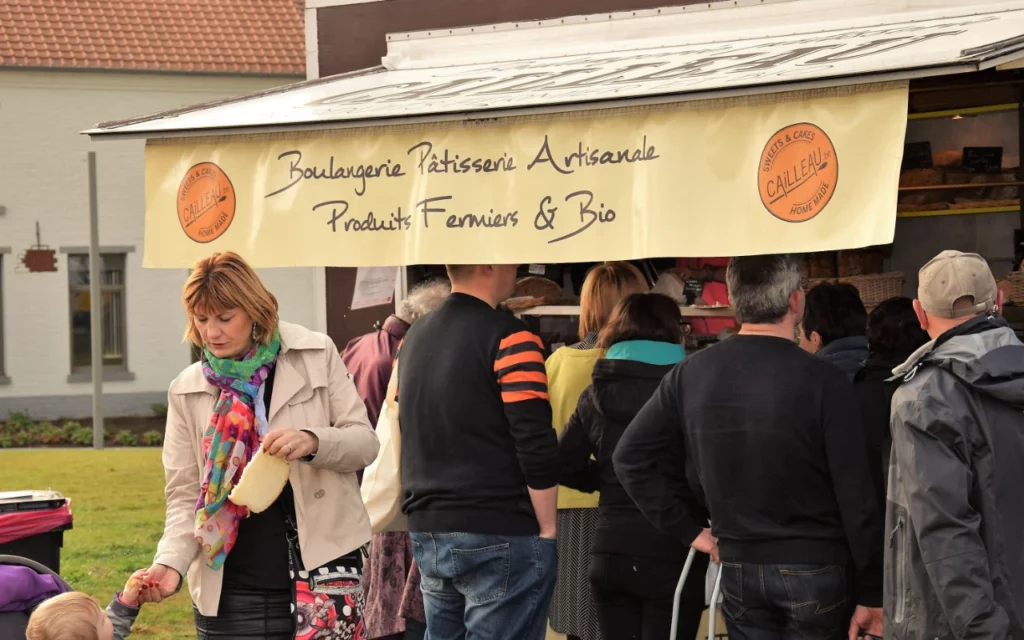 Des personnes qui font la file devant une remorque aménagée en échoppe pour vendre des produits fermiers et bio. Au premier plan, une maman qui donne une tranche de pain fraîchement acheté à son enfant