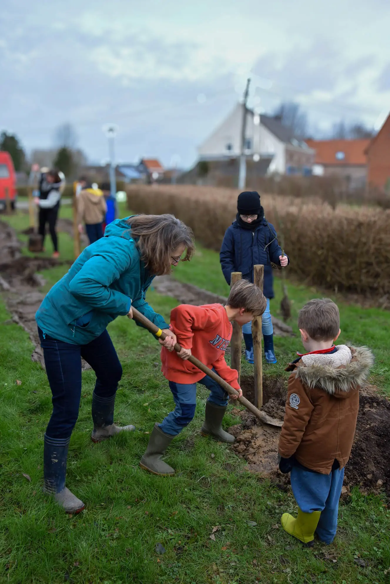 3 enfants aidés par une adulte pour creuser des trous afin de planter un arbre? Au second plan, flou, un autre groupe faisant la même chose.