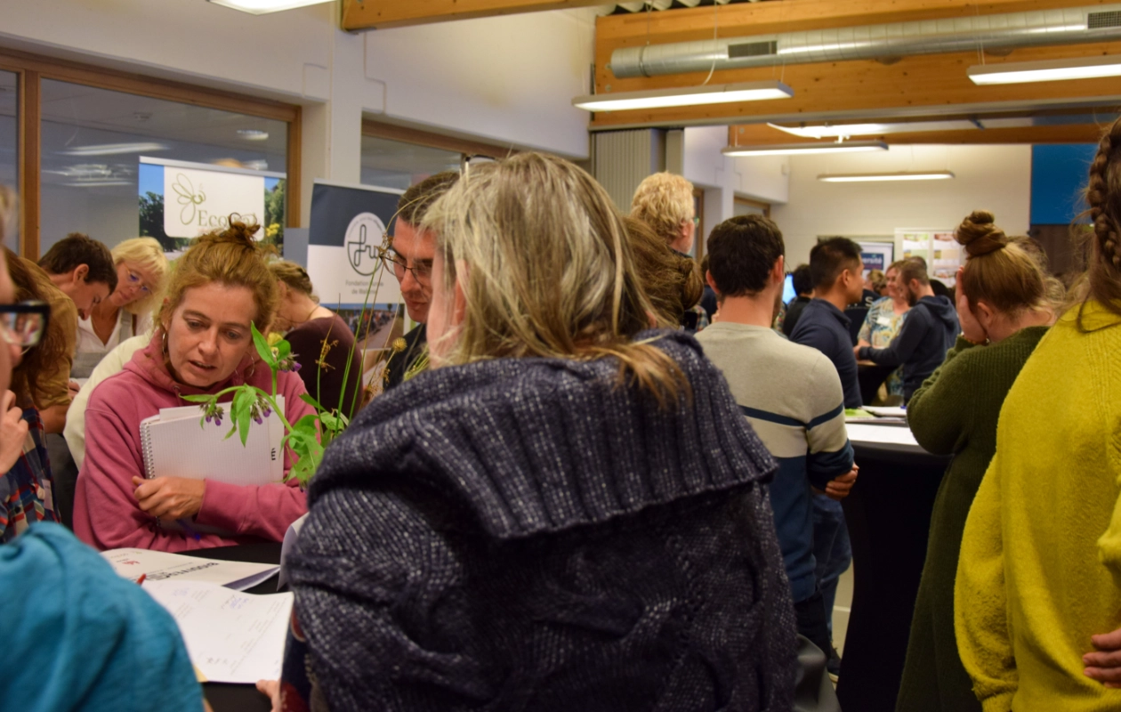 L'image montre les participants lors de la journée des Rencontres du Réseau BiodiverCité, rassemblés pendant le moment de réseautage. Les participants échangent en groupe autour des mange-debout, certains tenant des carnets ou prenant des notes.