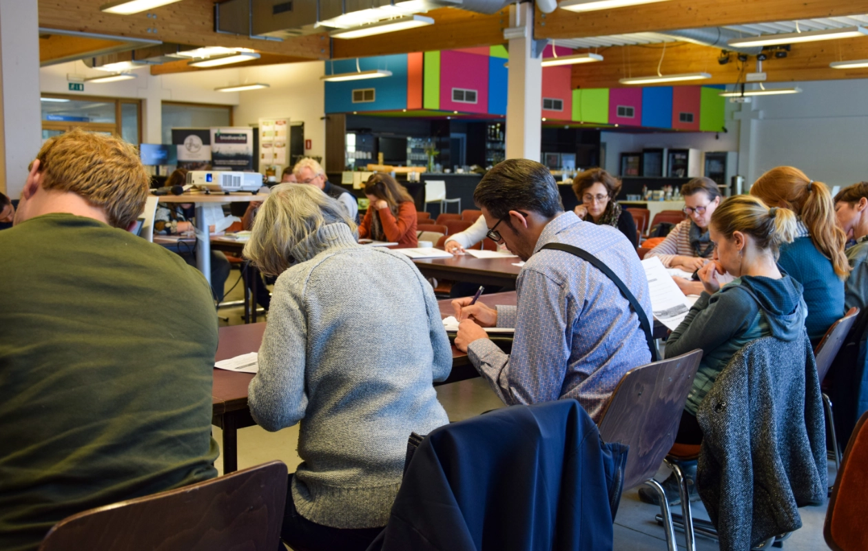 L'image montre différents participants de la journée des Rencontres du Réseau BiodiverCité se soumettant à un exercice lors de l'atelier sur le Naturascope. Les participants sont assis à des tables dans une salle, concentrés sur leurs tâches.