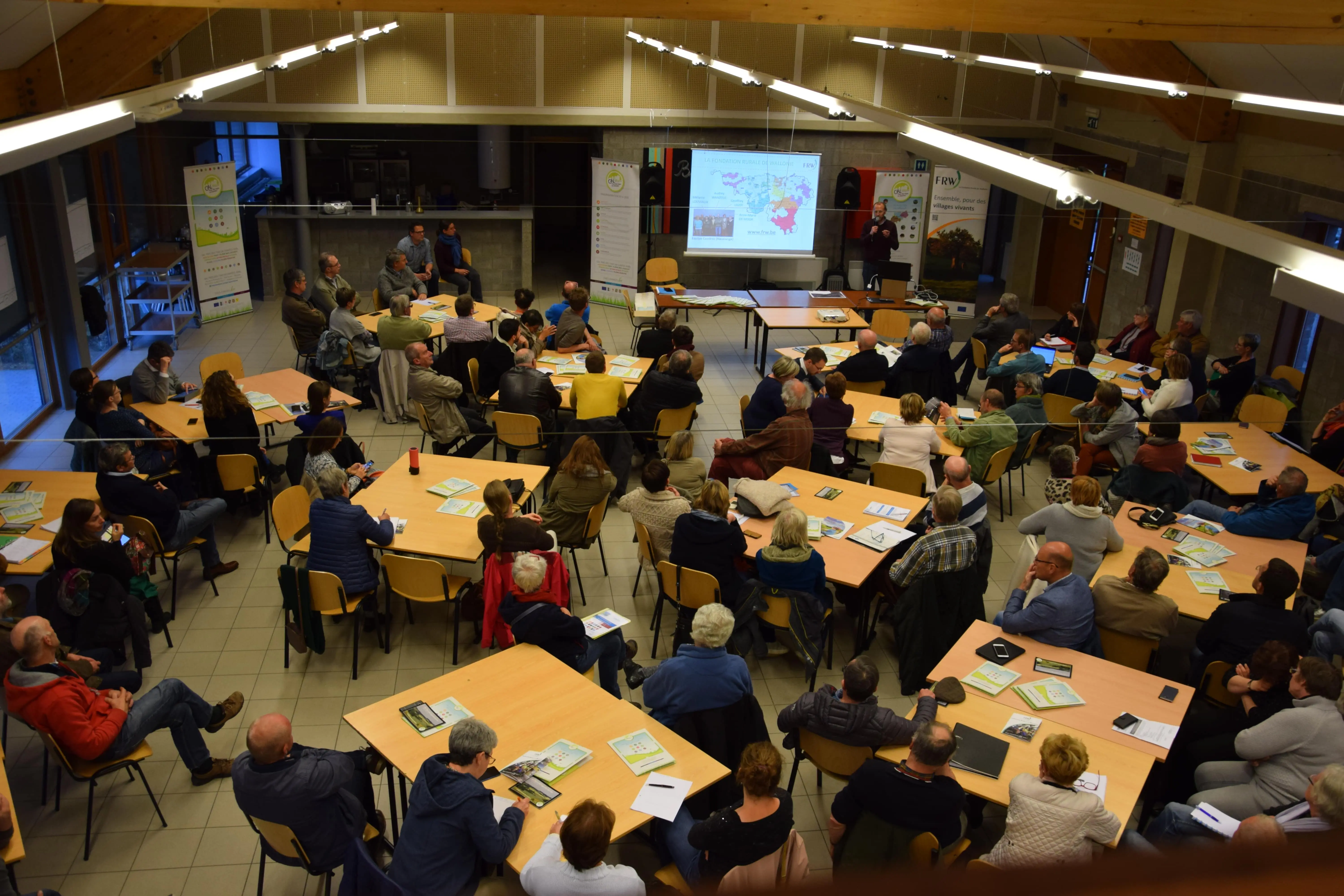 Une cinquantaine de personnes réparties sur plusieurs tables dans une salle et suivant une présentation sur le Vicigal