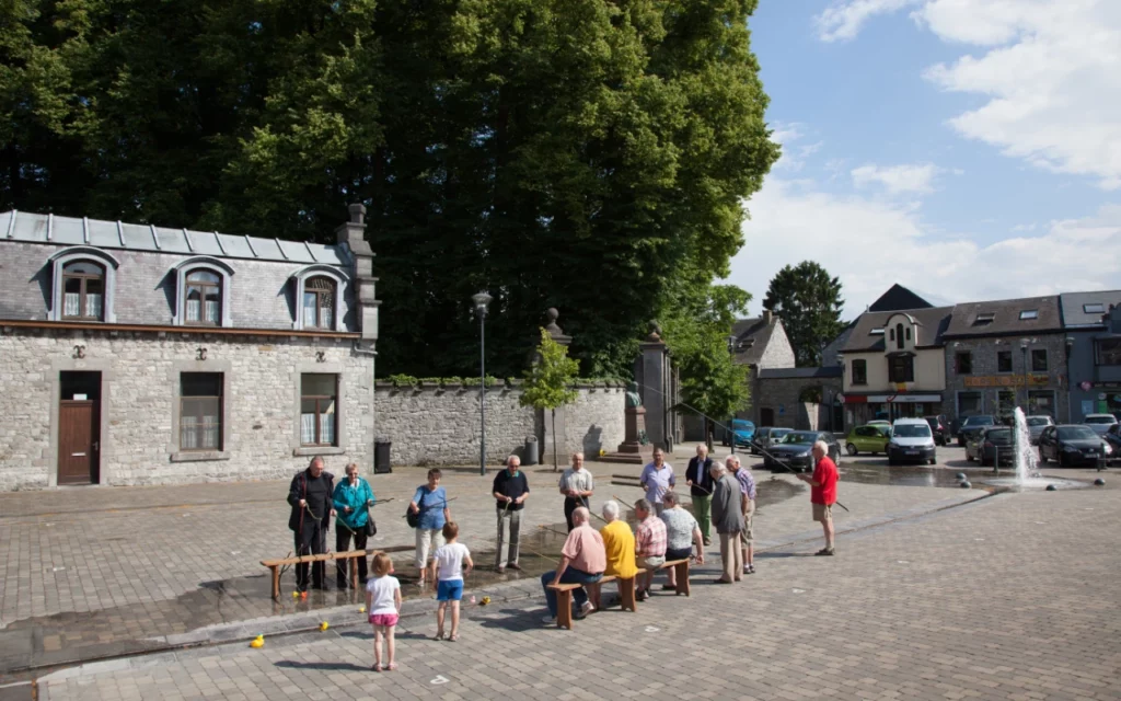 Une vingtaine de personnes âgées et 2 enfants participent à une pêche aux canards sur la place d'un village sous un soleil estival