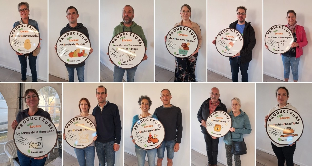 Onze personnes debout en rangée, chacune tenant un panneau circulaire avec des illustrations et du texte relatifs aux producteurs locaux de Somme-Leuze. Chaque panneau présente le nom d'un producteur ou d'une entreprise, ainsi que des images représentant leurs produits.