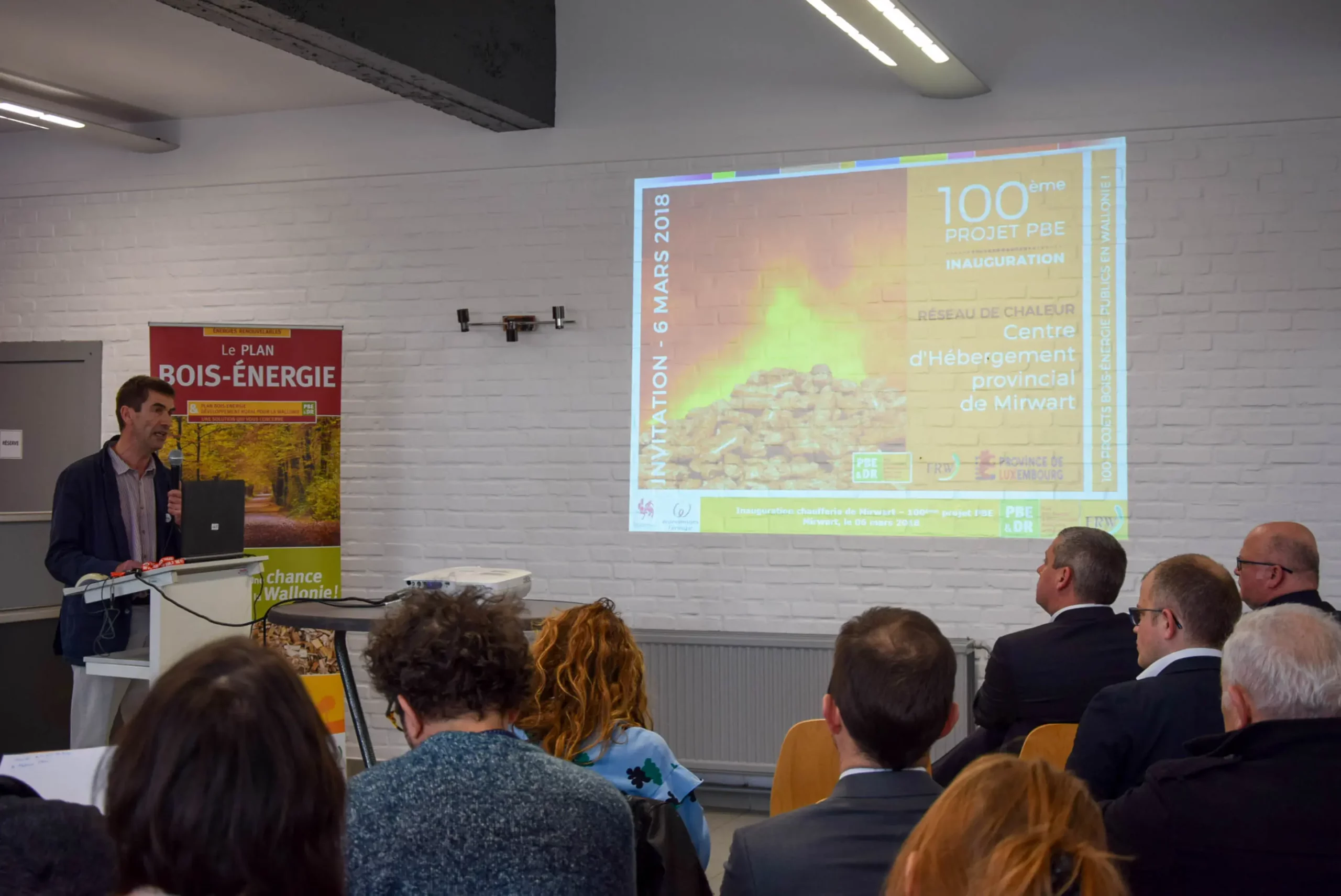 Des personnes, de dos et assises, qui assistent à la présentation du réseau de Chaleur de Mirwart lors de l'inauguration du projet.