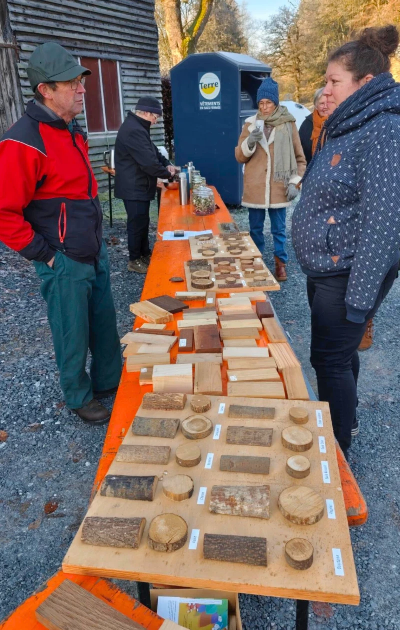 Stand du Groupe nature de Tenneville lors de la Semaine de l’Arbre, présentant différentes essences de bois et leurs usages sur une table orange.